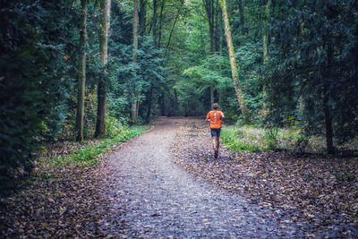 Man running on road amidst trees in forest