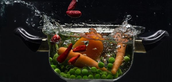 Food falling in container with water against black background