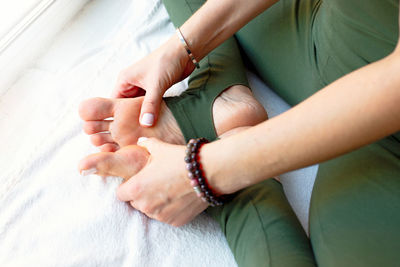 A slender woman in a green jumpsuit, in a yoga pose, clasping her legs with her hands