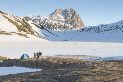 People walking on snowcapped mountain against clear sky