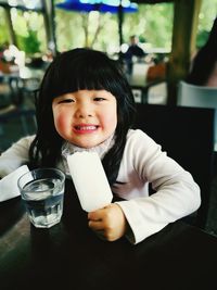 Portrait of cute girl having popsicle stick at table in restaurant
