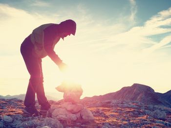 Man put last stone on peak of pyramid. balanced stacked stones on mountain summit. sunset above