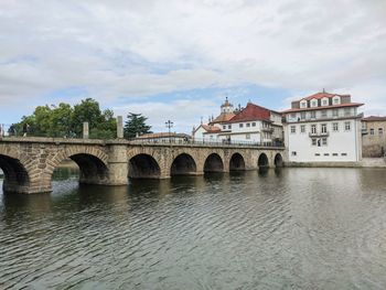 Arch bridge over river by buildings against sky