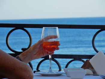 Close-up of hand holding glass against sea