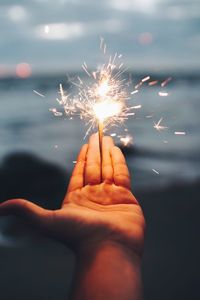 Cropped hand of person holding lit sparkler at night