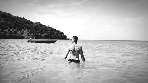 Full length of shirtless man in sea against sky