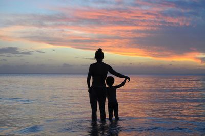 Rear view of silhouette of mother and son on beach against sunset sky