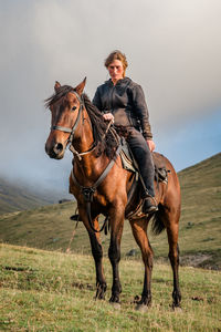 A cowgirl shepherd rider on a horse standing on a mountain valley on autumn day sky with clouds