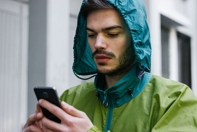 Close-up of man using phone while wearing raincoat