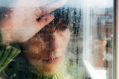 Melancholic young woman looking through window