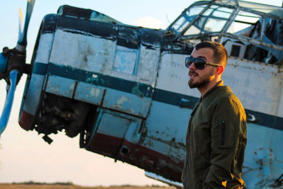 Side view of young man wearing sunglasses in front of airplane 