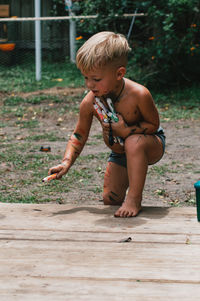 Full length of shirtless boy coloring on wood.