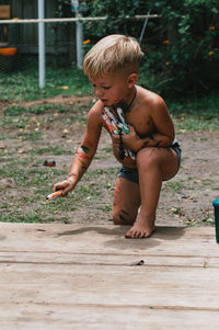 Full length of shirtless boy coloring on wood.