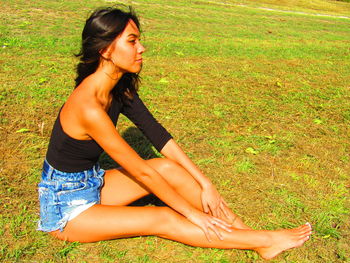 Side view of young woman sitting on field