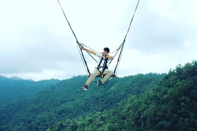 Low angle view of man hanging on rope against sky