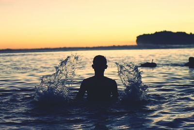 Rear view of silhouette man in sea against sunset sky