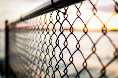 Close-up of chainlink fence against sky during sunset