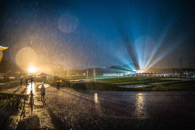 Rear view of people walking on illuminated street at night