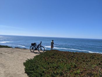 People riding bicycle by sea against clear blue sky