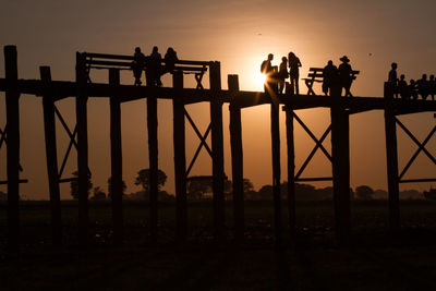 Low angle view of silhouette people on u bein bridge during sunset against sky