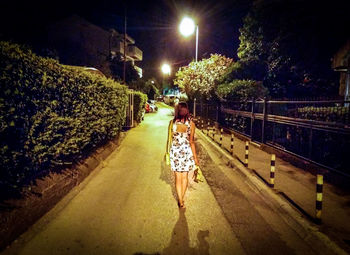 Rear view of woman walking on road at night