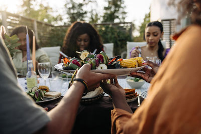 Friends passing snacks plate to each other during dinner party in back yard