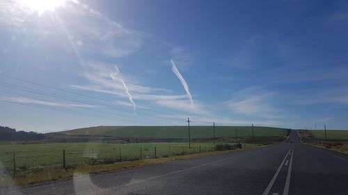 Country road amidst field against sky