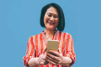 Low angle view of woman using mobile phone against blue background