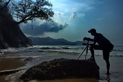 Man photographing at beach against sky