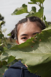 Close-up portrait of young woman by leaves outdoors