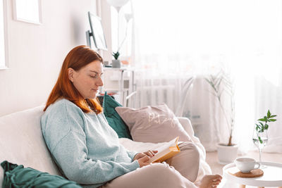 Young woman using mobile phone while sitting on bed at home