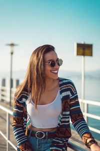 Smiling young woman wearing sunglasses standing against sky