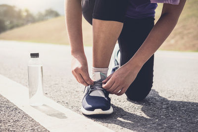 Low section of athlete tying shoelace on road during sunny day