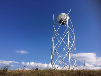 Low angle view of ferris wheel on field against blue sky