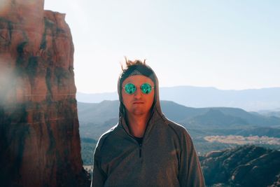 Portrait of young man wearing sunglasses while standing on mountain against sky