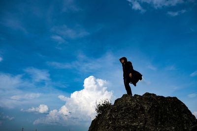 Low angle view of woman standing on rock against blue sky