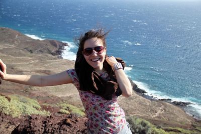 High angle portrait of young woman standing on cliff by sea