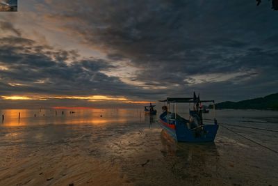 Boat moored on beach against sky during sunset