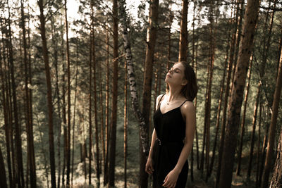 Young woman standing amidst trees in forest