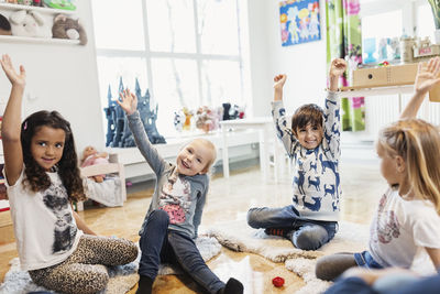 Happy children raising hands while sitting in preschool