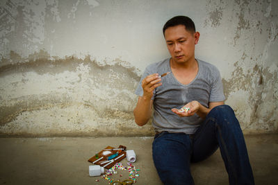 Man holding syringe while sitting against wall