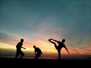 Silhouette men playing on beach against sky during sunset