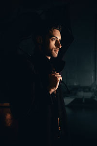 Young man looking away while standing outdoors at night