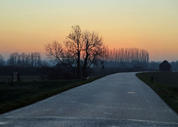 Road amidst bare trees against clear sky during sunset