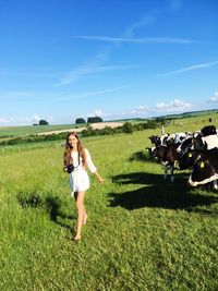 Portrait of woman with cows walking on field against sky