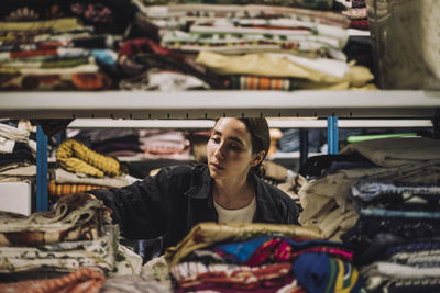 Female fashion designer searching clothes arranged on shelf at workshop
