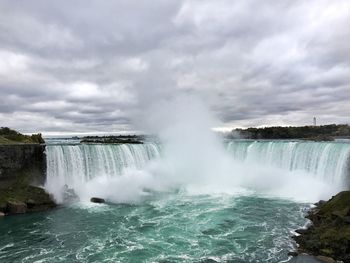 Scenic view of waterfall against cloudy sky