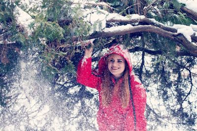 Portrait of smiling young woman standing against trees in winter