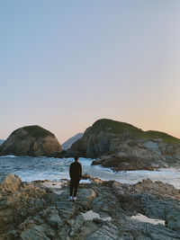 Rear view of man on rock at beach against clear sky