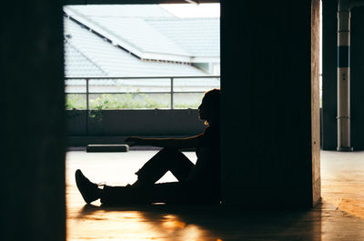 Low section of silhouette person sitting on wooden window